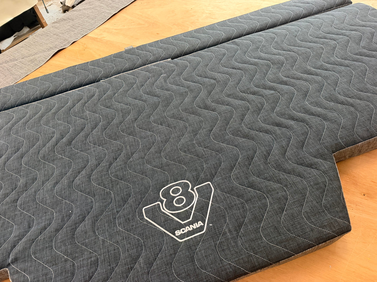 Two-part grey mattress topper for a Scania Next Gen sleeper cab pull-out bed, shown open with the V8 logo embroidered on the surface.